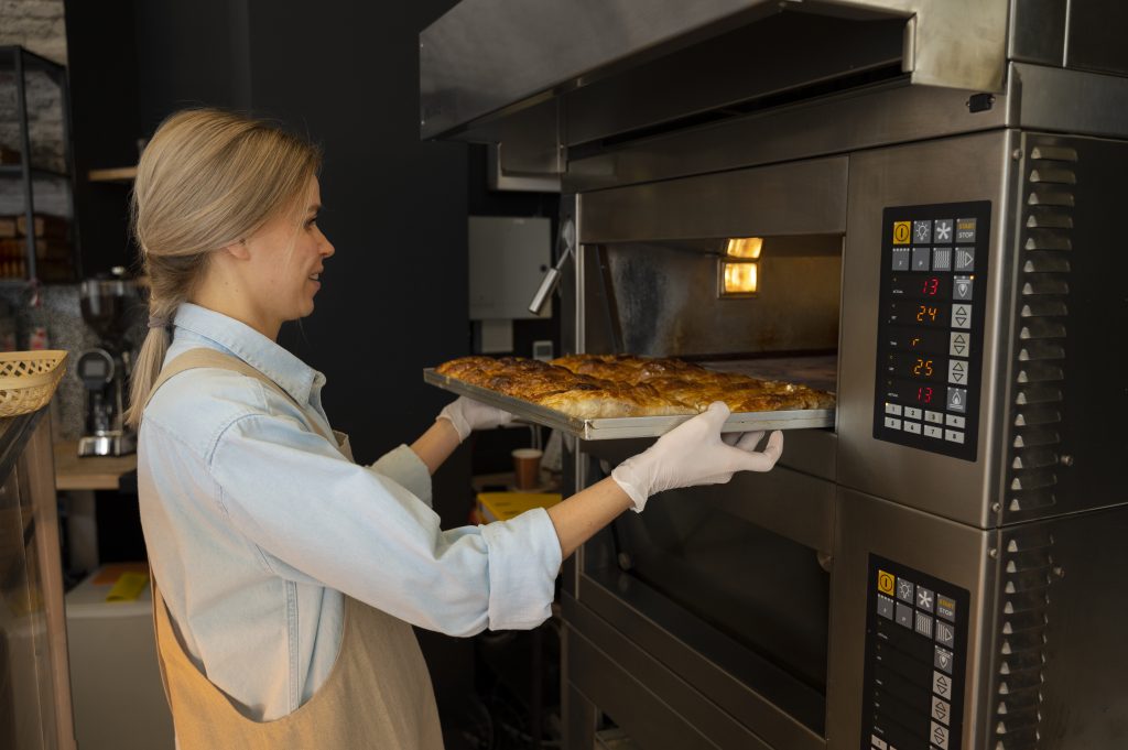 Image of a woman putting a tray of bread into the oven for baking in a bakery