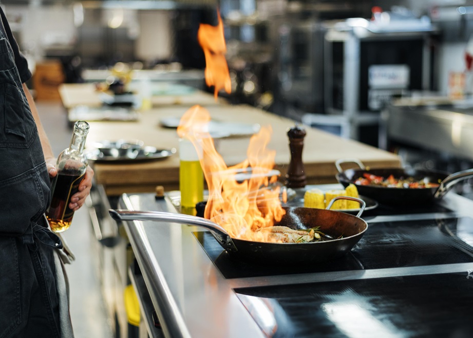 Chef flambeing food in a pan at a professional kitchen.