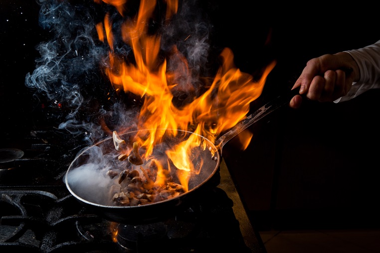 Chef performing a flambé cooking technique with a wok over a commercial induction cooker.