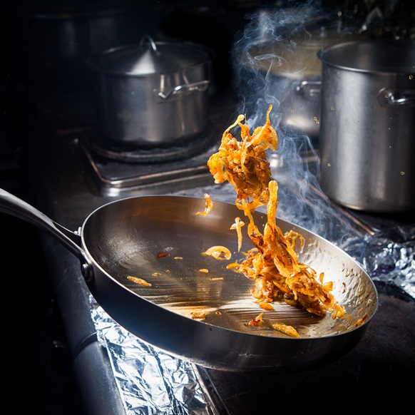 Sautéed food being tossed in a Commercial Induction Cooker with steam rising against a dark kitchen background.
